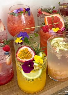 many different types of drinks are lined up on a wooden table with strawberries and flowers