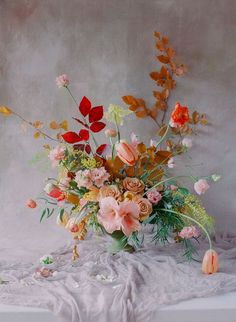 a vase filled with lots of flowers sitting on top of a white cloth covered table