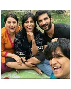 three people sitting on the ground smiling for a photo with another person standing next to them