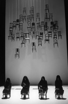 four people sitting on chairs in front of a wall with many chairs hanging from it