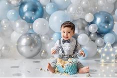 a baby boy sitting in front of balloons and cake