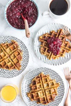 three plates with waffles and cranberry sauce next to two cups of coffee