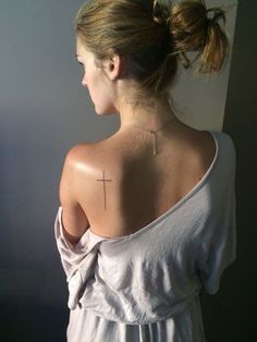 a woman with a cross tattoo on her upper back shoulder and behind her is a white dress