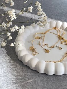 a white plate topped with lots of gold jewelry next to flowers on top of a table