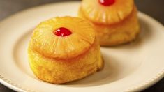 two small pineapples on a white plate with a red cherry in the middle