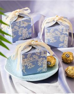 three blue boxes with gold foiled chocolates in them sitting on a white plate