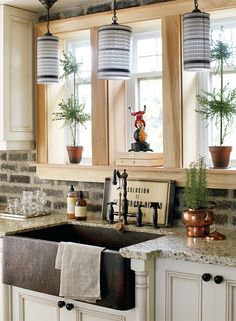 a kitchen sink under two hanging lights in front of a window with potted plants