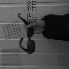 a pair of black sunglasses being held up by a woman's hand with chinese writing on the wall behind them