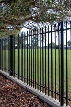 a black metal fence in the middle of a park with grass and trees behind it