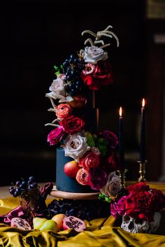 a table topped with a cake covered in flowers and fruit next to two lit candles