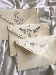 three envelopes with drawings on them sitting on a bed