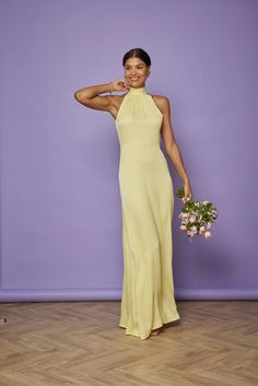 a woman in a long yellow dress holding a flower bouquet and posing for the camera