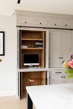 a desk with a computer on top of it next to a wall mounted cabinet in a kitchen