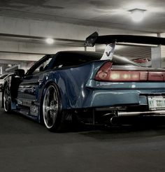 the back end of a blue sports car parked in a parking garage with lights on