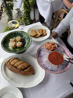 a table topped with plates and bowls filled with food next to wine glasses on top of a white table cloth