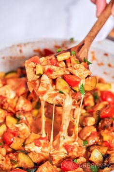 a wooden spoon full of chicken and vegetables being lifted from a skillet with a wooden spatula