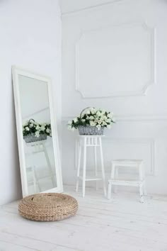 a white room with a mirror, stool and flowers in the basket on the floor