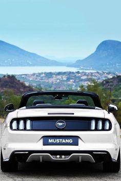 the front end of a white mustang parked on top of a dirt road with mountains in the background