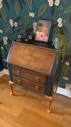 an old dresser with flowers painted on the wall behind it and a framed photo above it