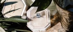 an engagement ring sitting on top of a box next to some flowers and greenery