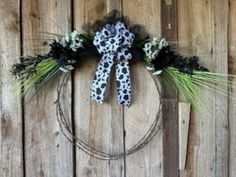 a wreath with an animal print bow hanging on the side of a wooden wall next to a fence