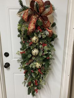 a christmas wreath hanging on the front door with bells and evergreens attached to it