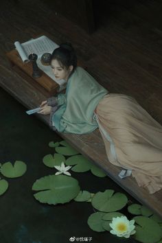 a woman is laying down on a bench next to lily pads and reading a book