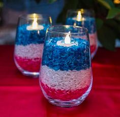 red, white and blue candles are sitting in glass vases on a tablecloth