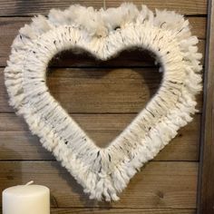 a white heart shaped wreath hanging on a wall next to a candle and some candles