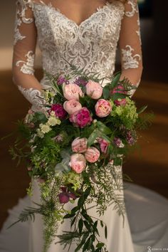 a woman in a wedding dress holding a bouquet of pink and green flowers on her arm