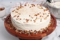 a cake with white frosting and nuts on a wooden platter next to other desserts