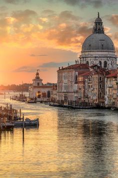 the sun is setting in venice, italy as boats are docked on the water and buildings line the shore