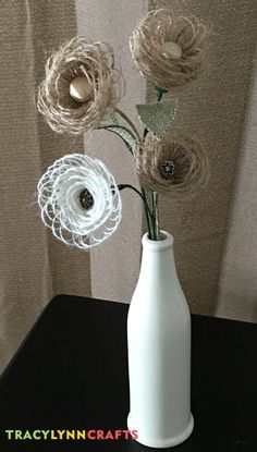 a white vase with some flowers in it on a black table next to a curtain