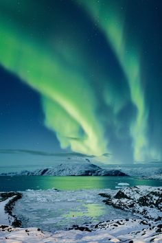 the aurora bore is shining brightly in the night sky over water and snow covered mountains