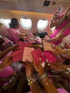 several women in pink dresses are sitting on an airplane and reaching out their hands to each other