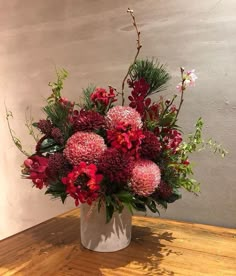 a white vase filled with red flowers on top of a wooden table next to a wall