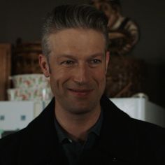 a man in a black jacket smiling at the camera