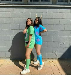 two young women standing next to each other in front of a brick wall wearing matching outfits