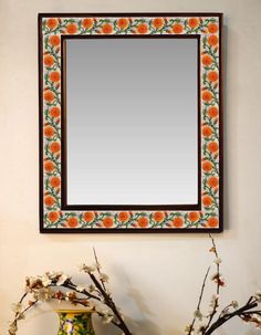 an orange and green vase sitting on top of a table next to a mirror above it