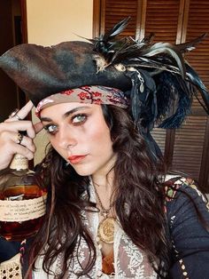 a woman wearing a pirate hat with feathers on her head and holding a bottle in front of her face