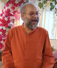 an old man with glasses and a beard is standing in front of a floral display