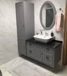 a white sink sitting under a bathroom mirror next to a gray cabinet and counter top