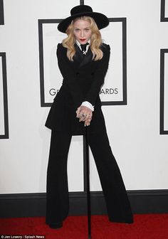 a woman in a black suit and hat holding a cane on the red carpet at an awards event