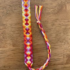 an orange, yellow and pink bracelet with a white bead on the end sitting on a wooden surface