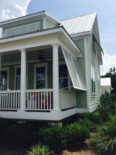 a house with white pillars and a porch on the front of it is surrounded by greenery