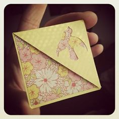 a hand holding an origami envelope with pink flowers on it and yellow paper