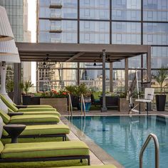 an outdoor swimming pool with lounge chairs and umbrellas in front of the building's glass windows