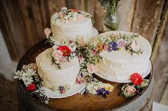 three tiered wedding cake on top of a wooden barrel with flowers and greenery