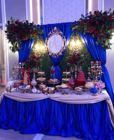 a table topped with lots of cakes and desserts next to a blue drapes