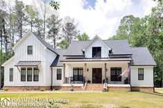 a large white house with black shutters and a flag on the front porch is surrounded by trees